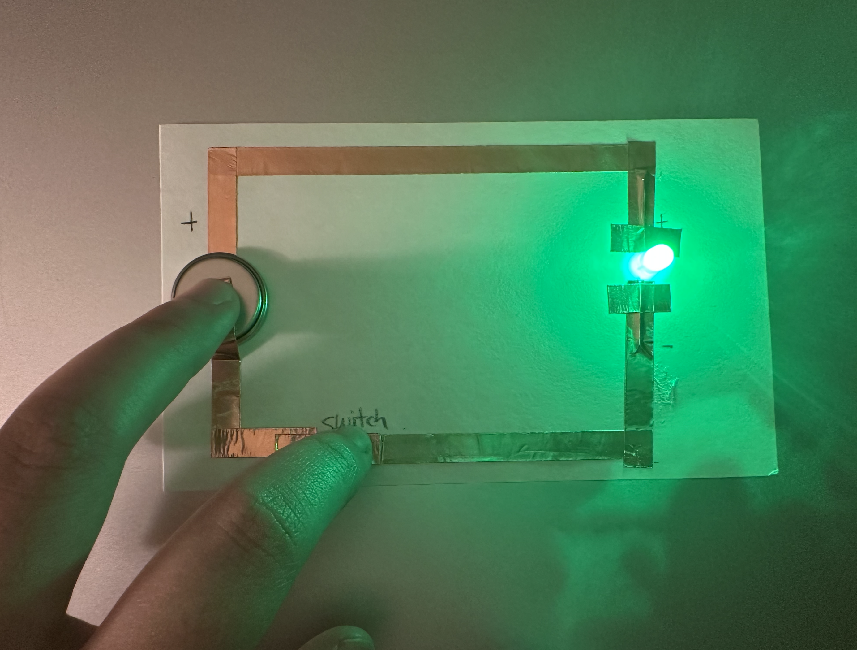 This image shows a simple circuit. I first drew a rough pencil sketch on paper and then placed copper tape on top. I noticed that leaving small gaps was necessary for the circuit to work. After placing the battery, the LED turned on.