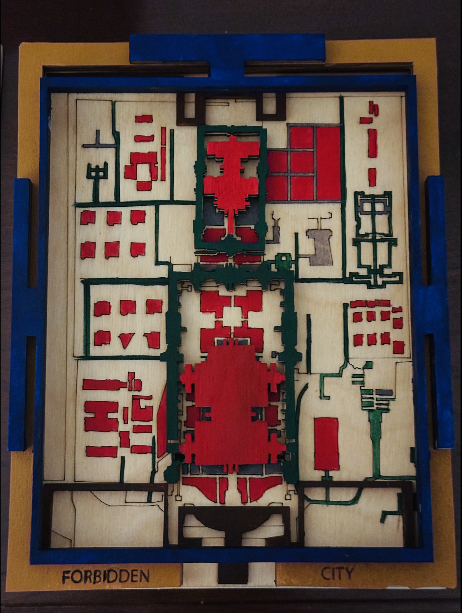 Multi layered laser cut of the Forbidden City made from engraved and fully cut wood panels.

  <p>The yellow outer frame represents the moat as a boundary rather than water.  </p>

  <p>The blue vase holds the 'water' that no longer exists outside and symbolizes the fragile inner life of the people who lived inside the palace.  </p>

  <p>The central halls are raised to show power and hierarchy.  </p>

  <p>The engraved base map reveals the full spatial grid of the Forbidden City and shows the palace as both a place of ceremony and a beautiful prison.